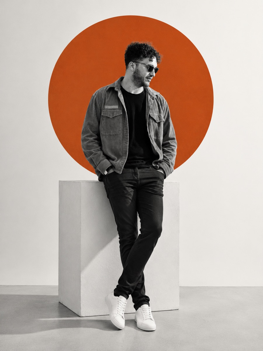 Kazim K., founder of K13 Software Studio, leaning on a plinth in front of a burnt-orange circle